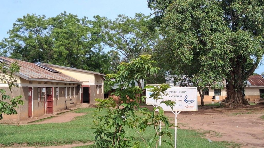 Classroom blocks and the Scripture Union sign under the big tree at Katrini Secondary School, Terego District